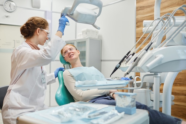 Paziente sdraiato sulla poltrona odontoiatrica e parlando con il dentista durante l'esame medico presso la clinica