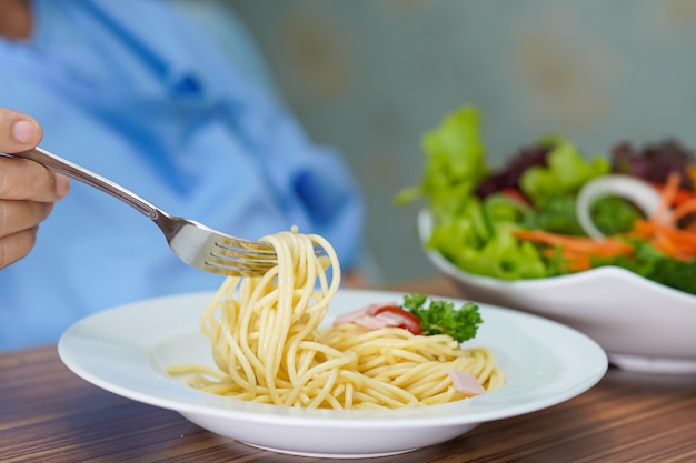 Paziente senior asiatico della donna che mangia gli spaghetti e l'insalata di carbonara.