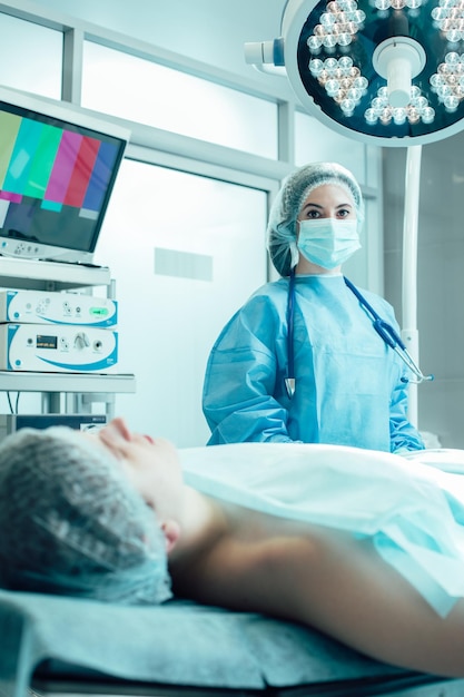Paziente su un lettino medico in sala operatoria. Giovane dottoressa con stetoscopio sul collo in piedi al suo fianco