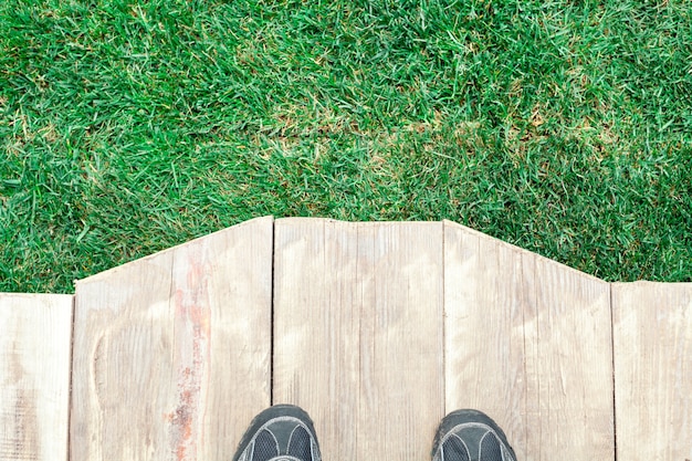 Pedana in legno con piedi ed erba verde come sfondo