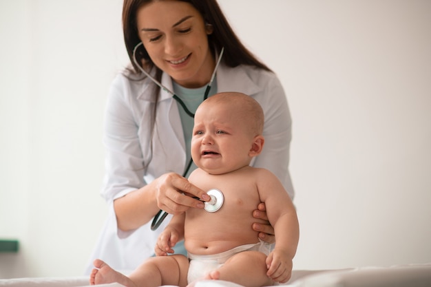 Pediatra di giovane donna che ausculta un neonato