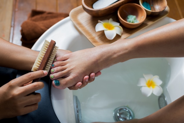 Pedicurista che pulisce il piede del cliente in ciotole per pedicure