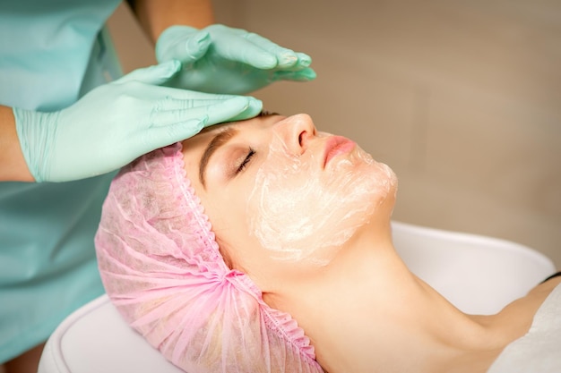 Peeling viso dall'estetista. Trattamento facciale. L'estetista applica alla paziente una maschera viso detergente.