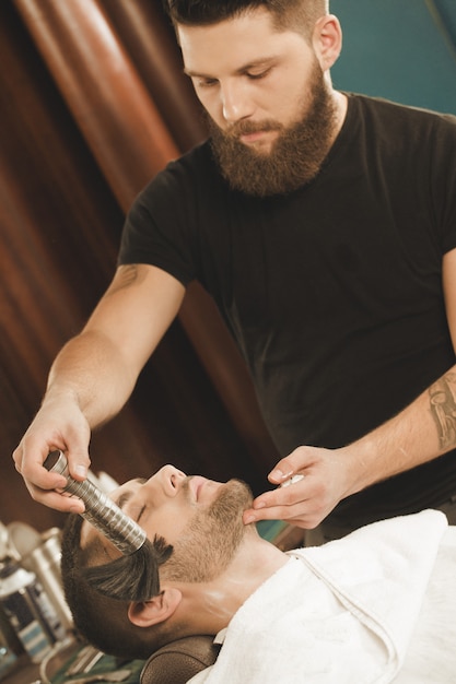 Pelle calmante dopo la rasatura. Barbiere barbuto professionista che applica polvere al viso del suo cliente usando il pennello da barbiere in polvere