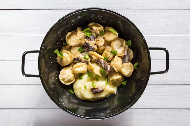 Pelmeni cibo russo, gnocchi di carne con salsa di funghi e purè di patate in ciotola nera.