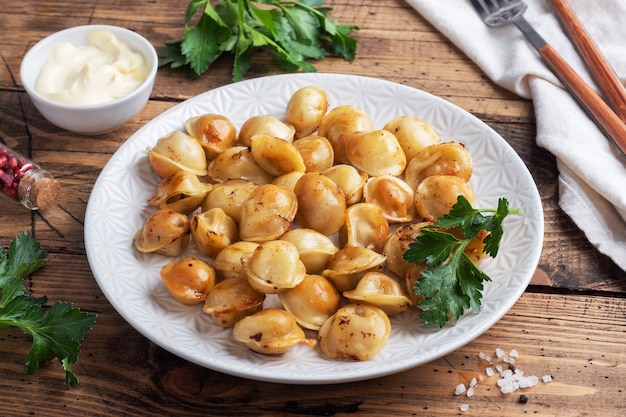 Pelmeni fritti tradizionali, ravioli, gnocchi ripieni di carne sul piatto, cucina russa. Tavolo rustico in legno, copia spazio.