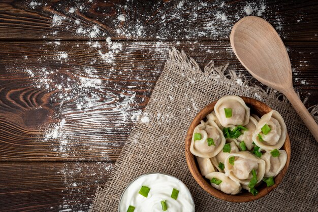 Pelmeni russi o gnocchi di carne con panna acida e cipolla verde su fondo di legno.