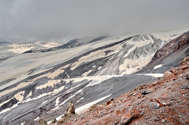 Pendii di montagna e roccia vulcanica nera ricoperta di neve. nuvole basse sulle cime solcate