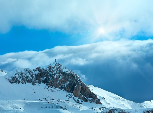 Pendio di montagna invernale con pista da sci e croce sulla cima della roccia (Austria).