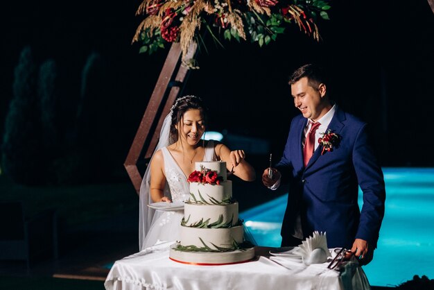 Pengantin baru dengan gembira memotong, tertawa, dan mencicipi kue pernikahan