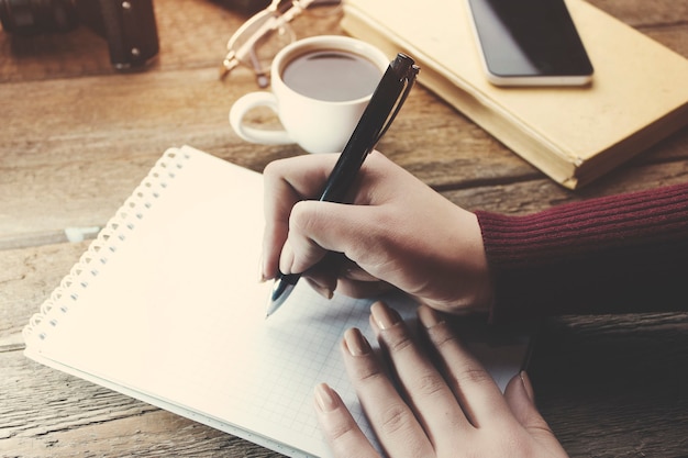 Penna della mano della donna che scrive sul taccuino sul tavolo di lavoro