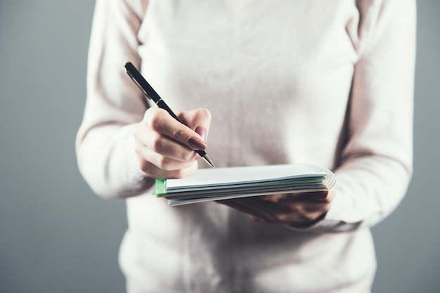 Penna della mano della donna con il blocco note su gray