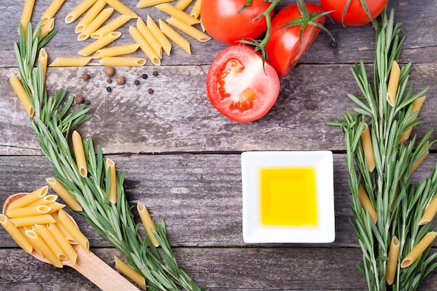 Penne al rosmarino, pomodori, olio d'oliva e pepe su un tavolo di legno