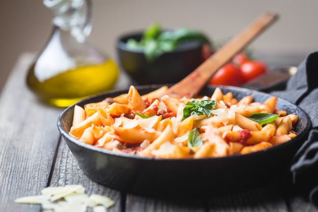 Penne al sugo di pomodoro e formaggio decorate con basilico su tavola di legno