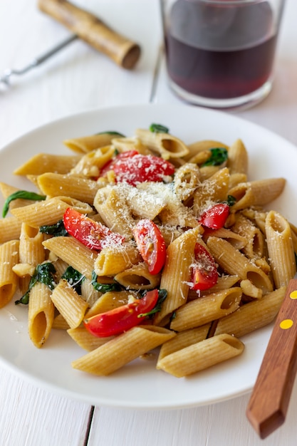 Penne all'italiana con pomodori, spinaci, parmigiano, aglio e noci. Mangiare sano. Cibo vegetariano.