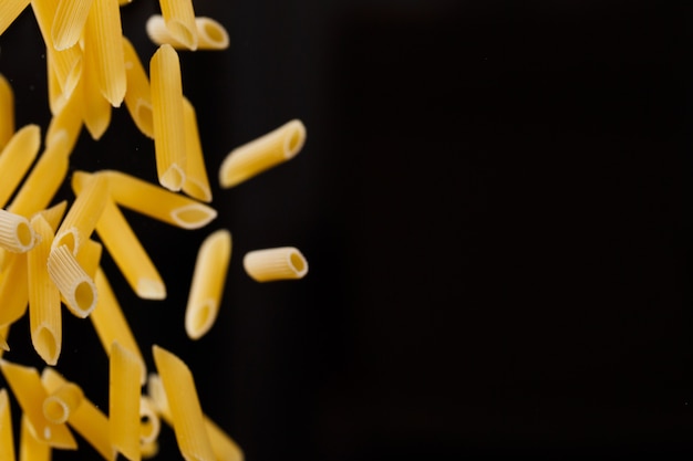 Penne che cadono. Maccheroni crudi gialli volanti su sfondo nero. Dof poco profondo.