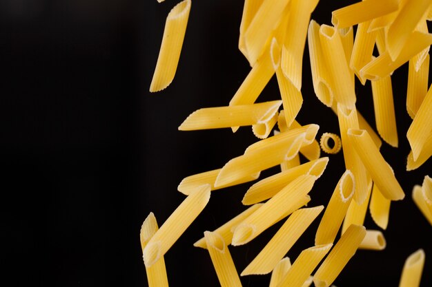 Penne che cadono. Maccheroni crudi gialli volanti su sfondo nero. Dof poco profondo.