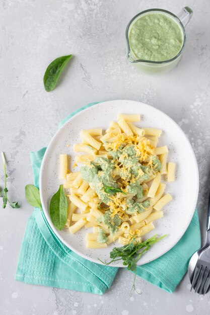 Penne con salsa di panna verde, formaggio e micro verdi su un piatto di ceramica