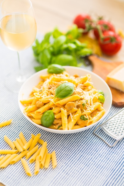 Penne di pasta con pezzi di pollo funghi basilico parmigiano e vino bianco. Alimento italiano in piatto bianco sul tavolo da cucina.