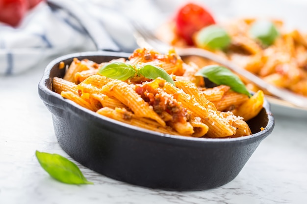 Penne di pasta e cibo italiano con salsa bolognese in padella.