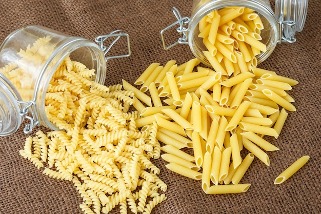 Penne e fusilli di pasta italiana in barattolo di vetro su fondo marrone