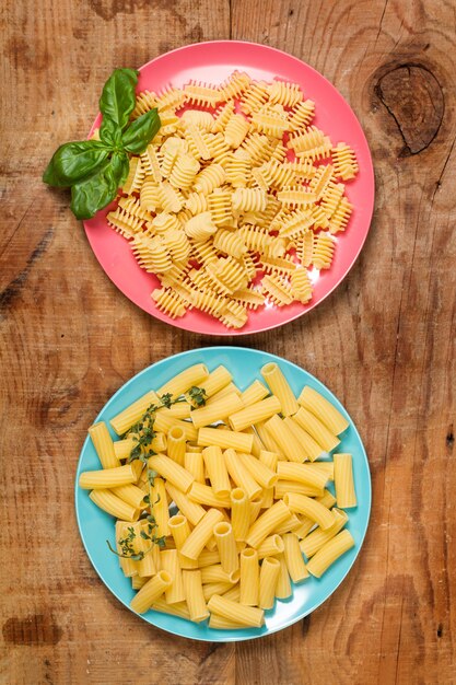 Penne e gnocchi secchi in due piatti colorati su un tavolo di legno