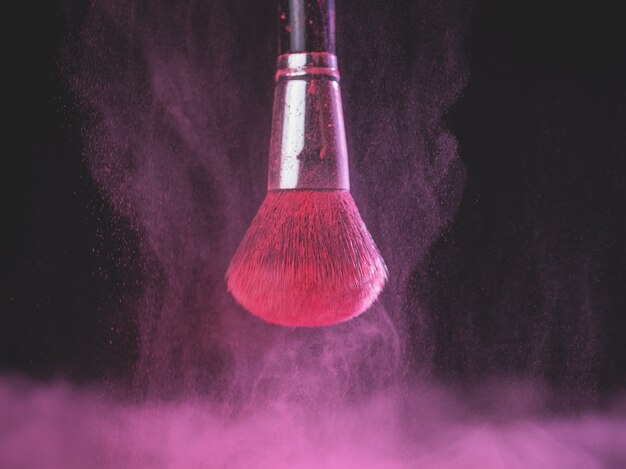 Pennello da trucco con esplosione di polvere rosa su sfondo nero