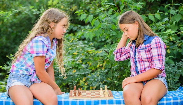 Pensa meglio. Le bambine giocano a scacchi. Sorelle che giocano a scacchi. Bambini intelligenti. Sviluppo della prima infanzia. Gioco intellettuale. I bambini giocano a scacchi all'aperto sullo sfondo della natura. Sport e concetto di hobby.