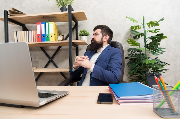 Pensando all'obiettivo principale Uomo barbuto capo seduto in ufficio con laptop Manager che risolve problemi aziendali Uomo d'affari responsabile delle soluzioni aziendali Sviluppo di una strategia aziendale Affari rischiosi