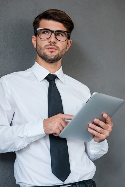 Pensando alla soluzione. Fiducioso giovane in camicia e cravatta che tiene tablet digitale