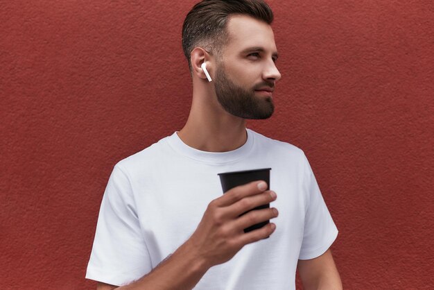 Pensando alla vita bell'uomo barbuto in cuffia con in mano una tazza di caffè e guardando da parte