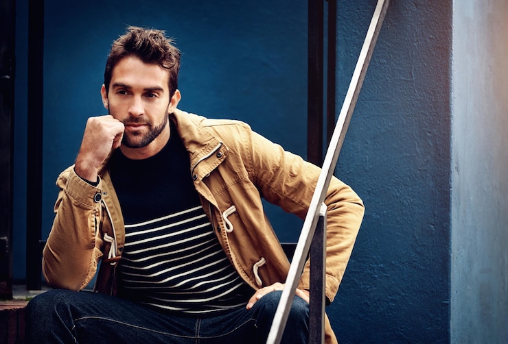 Foto pensare alla moda e un uomo in città su uno sfondo a parete blu per lo stile di abbigliamento alla moda idea di viso e una giovane modella in un abito vestito seduto sulle scale in una città urbana durante il giorno