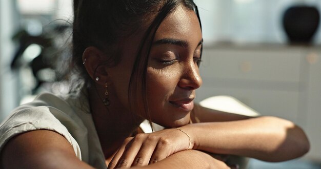 Pensare calma e giovane donna su un divano rilassarsi con un'idea o un ricordo in soggiorno sorriso di pace e felice persona femminile indiana chilling nel salotto di un appartamento moderno per respirare