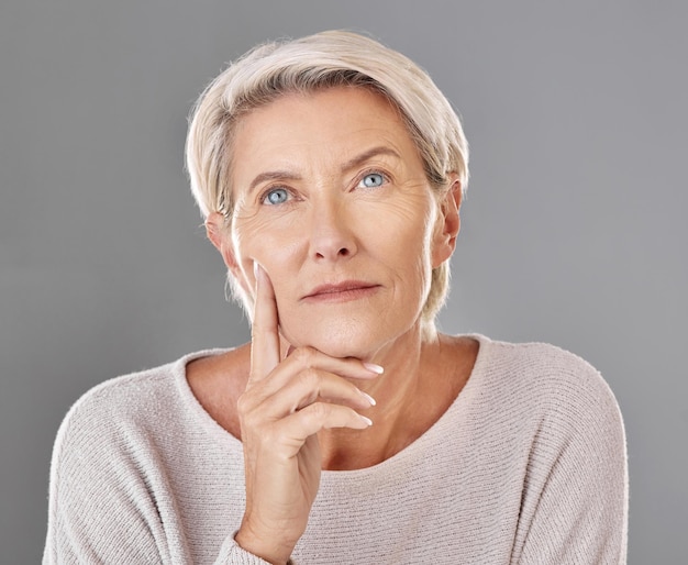 Pensiero maturo e donna che tocca il viso in uno sfondo grigio isolato per studio