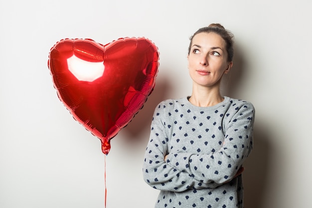 Pensieroso giovane donna in un maglione e un cuore in mongolfiera su uno sfondo chiaro. Concetto di San Valentino. Banner.