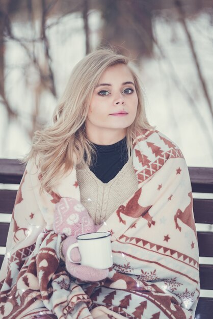 Pensieroso relax e ragazza felice con una bevanda calda seduta nella foresta invernale.