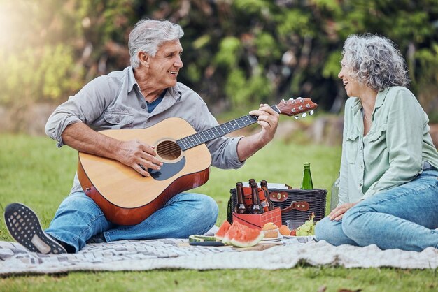 Pensionamento amore e chitarra con coppia in picnic nel parco insieme per rilassarsi estate o cibo Natura benessere e felice vecchio e donna che ascoltano musica in campagna campo per la salute in primavera