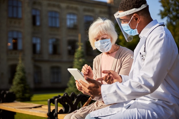 Pensionato assonnato che si siede e dà un'occhiata al tablet mentre ascolta le spiegazioni del medico specialista