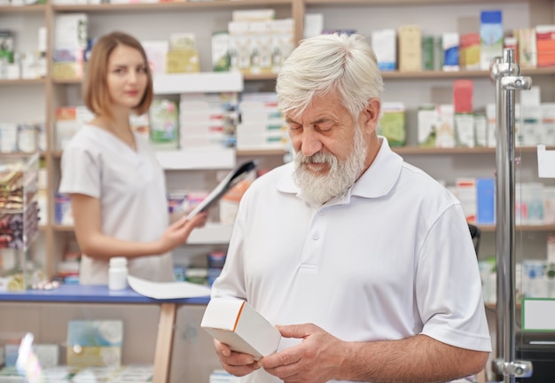 Pensionato che sceglie medicinale in farmacia.