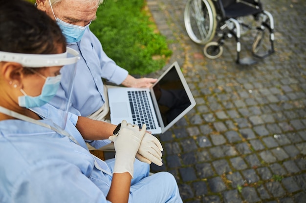 Pensionato che tiene il computer sulle ginocchia con il medico seduto vicino a lui