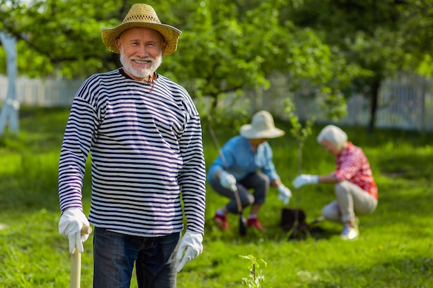 Pensionato sorridente. Bello pensionato dai capelli grigi che sorride mentre lavora in giardino con gli amici