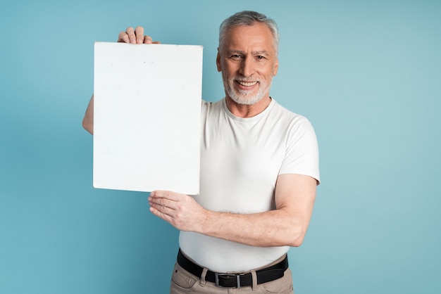 Pensionato sorridente con la barba che tiene un foglio di carta bianco