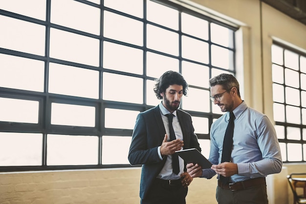 Penso che tu sia partito bene Inquadratura di due uomini d'affari ben vestiti che fanno brainstorming insieme su un tablet nel loro ufficio