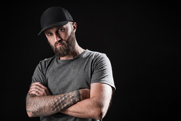 Pensoso uomo nero con la barba vestito con una camicia grigia, occhiali da sole e berretto da baseball.