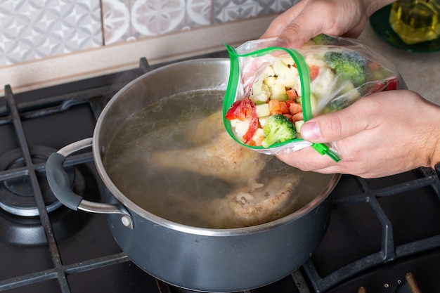 Pentola con brodo e verdure surgelate sul fuoco. Brodo d'osso. Brodo di pollo