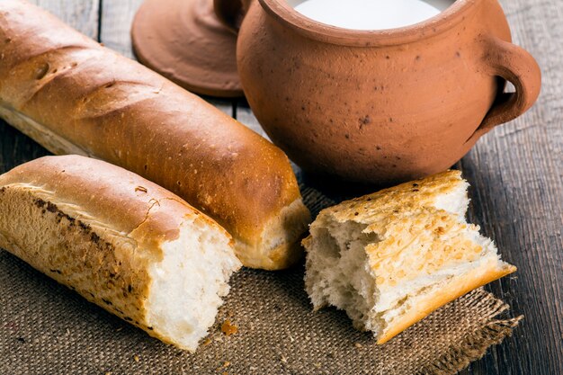 Pentola di terracotta con latte e baguette su tavola di legno