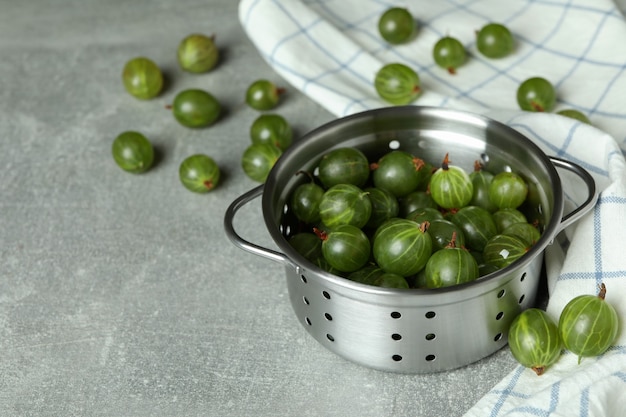 Pentola di uva spina matura e asciugamano da cucina sul tavolo strutturato grigio