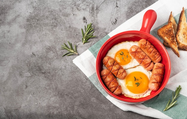 Pentola rossa con le uova fritte e le salsiccie su gray