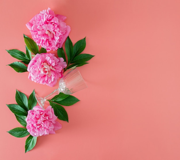 Peonia rosa fresca con foglie verdi e bicchiere di vino su sfondo rosa pastello con spazio per le copie. piatto estivo tropicale minimo disteso con spazio di copia. sfondo minimo del giardino.