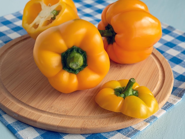 Peperoncini gialli colorati sulla tavola da taglio e asciugamano di lino blu e bianco su un tavolo di legno rustico Peperoncini dolci freschi Composizione colorata e elegante Alimento sano vegetariano